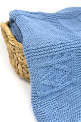 Blue wool textured knitted blanket in a basket on a white background close up,