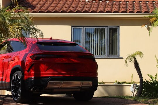 Red sports car in driveway tropical island / Vacation mansion with supercar. Real estate and sports cars in L.A. Sports Car wallpaper, sleek red car. Car and mansion background image for web design. 