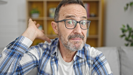 Obraz premium Middle age man sitting on sofa with i don't know expression at home