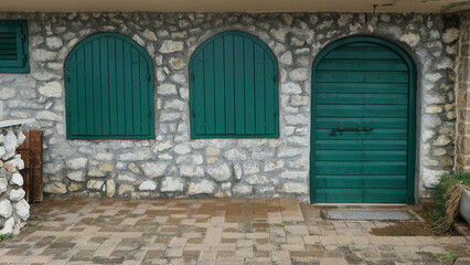 two green arched windows next to old green door with arched frame and against stone wall