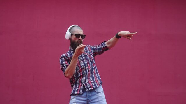 Stylish guy with headphones dancing on the background of a red wall on the street.