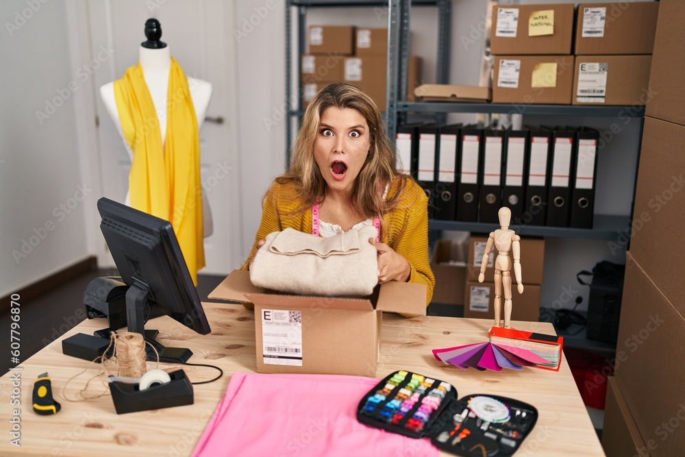 Canvas Prints Young woman by manikin at small business packing order afraid and shocked with surprise and amazed expression, fear and excited face.