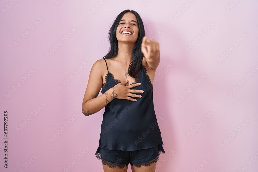 Poster brunette woman wearing black pajama laughing at you, pointing finger to the camera with hand over bo