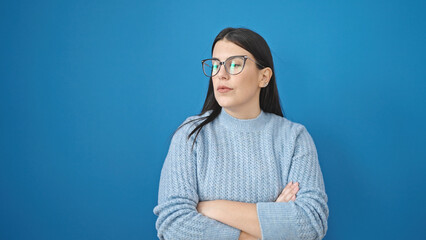 Young hispanic woman standing with arms crossed gesture looking serious over isolated blue background