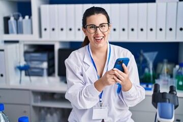 Young hispanic woman scientist using smartphone working at laboratory