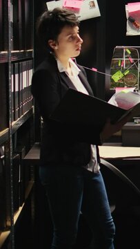 Vertical video Law agent examines confidential records, trying to identify suspect on surveillance photos. Investigator gathering intelligence with forensic sicence report, detective inspector.