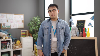 Young chinese man teacher standing with relaxed expression at kindergarten