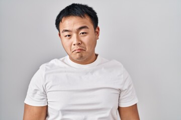 Young chinese man standing over white background depressed and worry for distress, crying angry and afraid. sad expression.