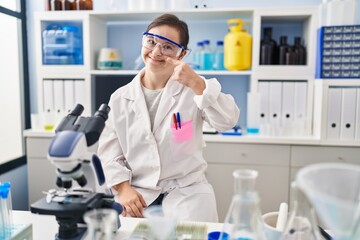 Fototapeta premium Hispanic girl with down syndrome working at scientist laboratory pointing with hand finger to face and nose, smiling cheerful. beauty concept