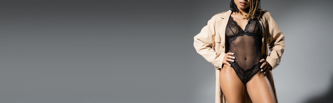 Partial View Of Graceful And Sexy African American Woman In Fashionable Beige Trench Coat And Black Lace Lingerie Posing With Hands On Hips On Grey Background, Banner