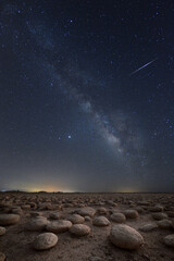 filed of round stones during the night with a milky way in the background and a falling star 