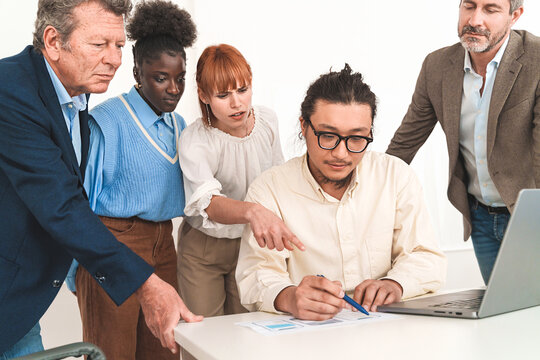 Diverse team working on mobile app design, with a Chinese developer showing wireframes. Caucasian woman points at drafts.
