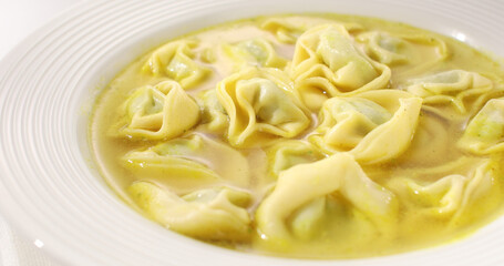 Pasta tortelloni with ricotta and spinach in chicken broth. hot italian pasta on a white plate. ready to eat food. sunny day. angle view. 
