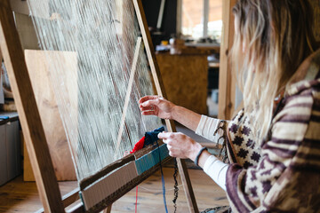 Crafty woman weaving at a loom at her workshop
