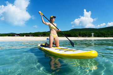 Woman stand up on paddle board in sea. Big yellow board in turquoise water.