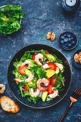 Yummy salad with fresh strawberry, shrimps, arugula, avocado and red onion, blue stone table. Fresh useful dish for healthy eating