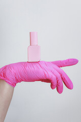A manicurist wearing gloves holds gel polish on a white background