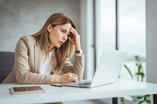 Shot of a young businesswoman looking stressed out while working in an office. Stressed business woman working from on laptop looking worried, tired and overwhelmed