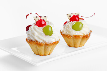 Beautiful cream cakes with cherries and grapes on a plate on a white background