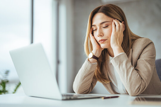 Female entrepreneur with headache sitting at desk. Businesswoman under terrible physical tension at work. Business woman with hands on her face looking exhausted