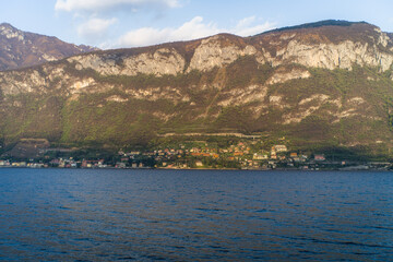 Fototapeta na wymiar Lake Como from the shore of the town of Bellagio. View of the Alps mountains, buildings and a passenger ferry. Sunset