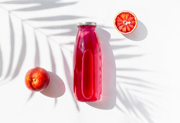 Creative still life flat lay made of a bottle with homemade citrus kombucha on white background with palm tree leaf shadow and blood orange fruit. Minimal style. Healthy beverege concept