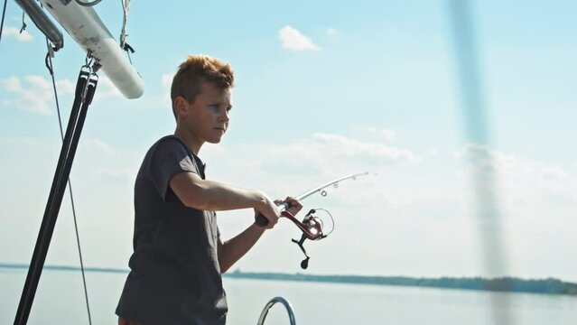 Teen boy spending sunny summer day on sailing yacht casting fishing rod into lake water