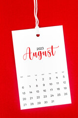 The August 2023 calendar page for 2023 year hanged on white rope on Red background.