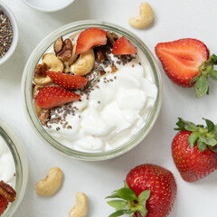 Greek yogurt, nuts and strawberries in a glass jars on a white table top view