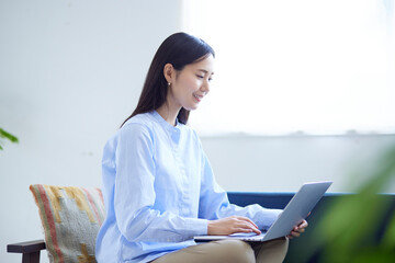 リビングのソファーでパソコンを操作する日本人女性の夏のイメージ