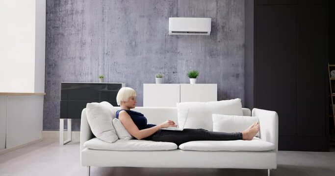 Woman Lying Under Air Conditioner On Couch Using Laptop