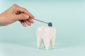 Dentist hand holding a dentist mirror and a healthy white tooth model on a blue background. Copy...