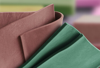 close up of thin brown and green foam materials in an blurry warehouse room. folded material sample sheets