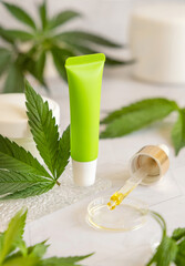 Green Blank Cream tube near cannabis leaves on white table. Cosmetic Mockup