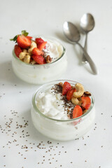 Greek yogurt, nuts and strawberries in a glass jars on a white table close up, copy space