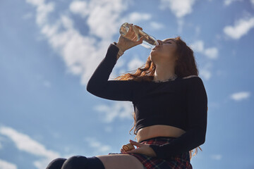 Roller blader woman drinking fresh water from a reusable glass bottle in a skatepark. Portrait of young adult female skater hydrating after a ride