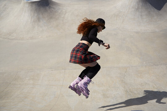 Female roller blader jumping in a skate pool outdoor. Young adult skater in aggressive inline skates riding in a concrete bowl in summer