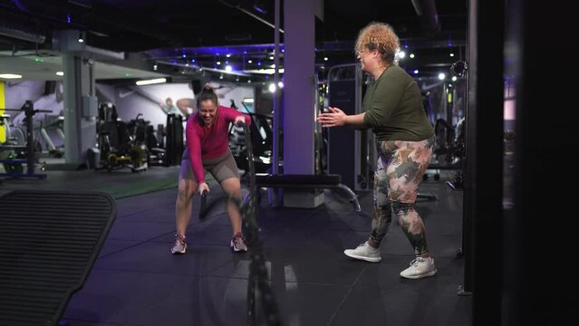 Two beautiful, overweight women push their limits during a workout, supporting each other every step of the way on their journey toward improved health and fitness. Using battle rope.	
