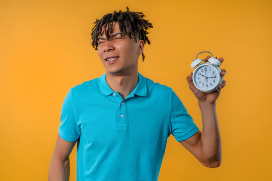 Woken up by alarm clock sleepy african man holding it in hand. Yellow background