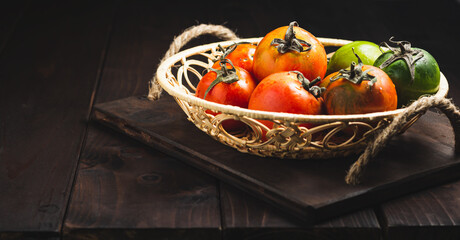 Still life of fresh colorful ripe fall or summer heirloom variety tomatoes in a basket on dark...
