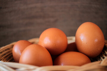 Close-up view of raw chicken eggs in egg basket on brown wooden background