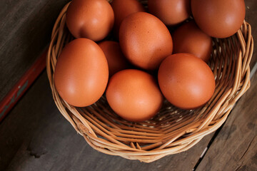 Close-up view of raw chicken eggs in egg basket on brown wooden background