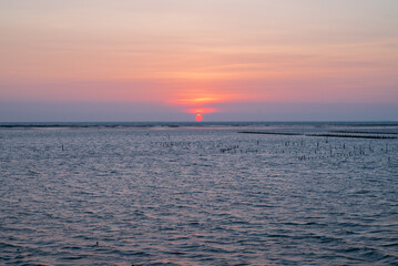 Fototapeta premium The sun was just falling below the horizon during golden hour. The quite beautiful sunset at Tainan quigu of Taiwan. The sky shines fantastic orange hue and the sea has the wonderful reflection.