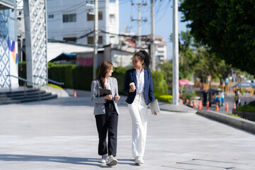 Two young female accountants walk and talk in front of the building's office. Corporate colleagues discussing new projects while going to work outdoor business