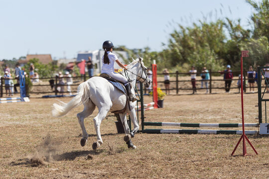 Equestrian sport - a little girl in uniform riding white horse at the ranch - jumping over the obsticles