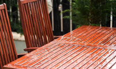 Close up photo during a rain over a wooden garden table. Outdoor backyard landscape during a summer rain.