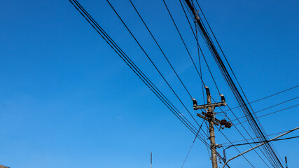 Electric wires and electric poles crossing the high voltage pole tower against the blue sky background.