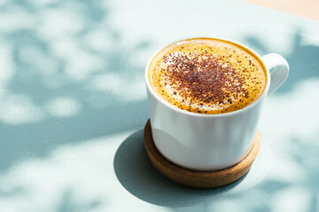 Top view of cup cappuccino coffee decorated with powder on blue table with beautiful shadows