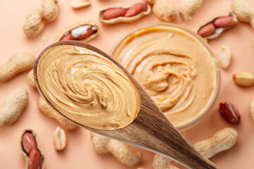 Wooden spoon with peanut butter. Peanuts lay on beige at the background. Top view.