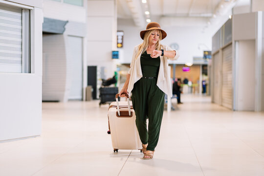 Focused elderly woman with suitcase checking time on wristwatch in airport